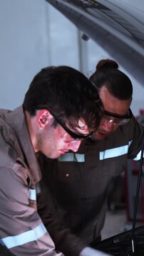 Two experienced automotive technicians work together while inspecting a vehicle engine inside a modern repair garage. The image represents teamwork, collaboration, technical expertise, diagnostics, pr