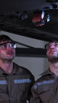 Two experienced automotive technicians work together while inspecting a vehicle engine inside a modern repair garage. The image represents teamwork, collaboration, technical expertise, diagnostics, pr