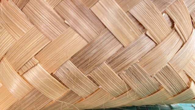 A detailed, close-up shot of a traditional woven bamboo texture showing intricate handcrafting, diagonal interweaving patterns, and natural light-brown wooden fibers. Ideal for background designs, cra
