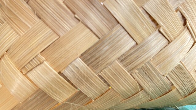 A detailed, close-up shot of a traditional woven bamboo texture showing intricate handcrafting, diagonal interweaving patterns, and natural light-brown wooden fibers. Ideal for background designs, cra