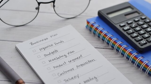 Close up of checklist on notepad with calculator and glasses on desk for business planning footage