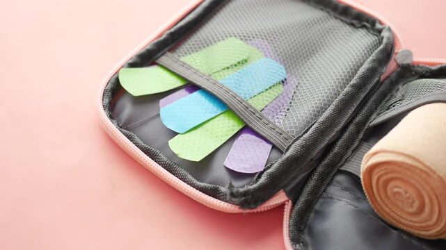 Colorful medical bandages and elastic wrap in pink first aid kit bag on pastel background