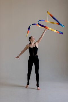 Young rhythmic gymnast girl performing routine with colorful ribbon in studio
