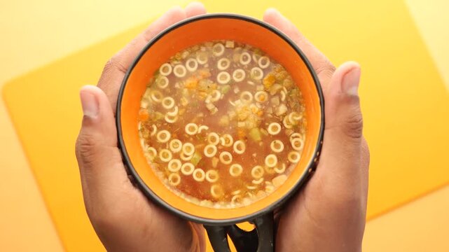 Close up of person holding bowl of warm vegetable soup with tiny ring pasta