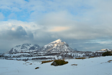 Scenic winter landscape of snow covered plains and majestic mountain peaks in Lofoten Islands, Northern Norway. Beautiful Arctic nature scenery under cloudy sky during a Scandinavian road trip travel  © bank215
