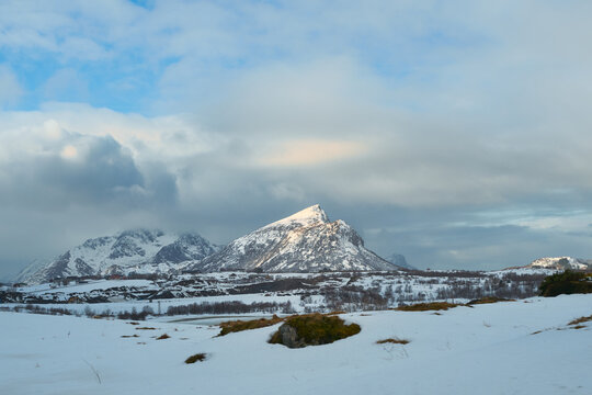 Scenic winter landscape of snow covered plains and majestic mountain peaks in Lofoten Islands, Northern Norway. Beautiful Arctic nature scenery under cloudy sky during a Scandinavian road trip travel 