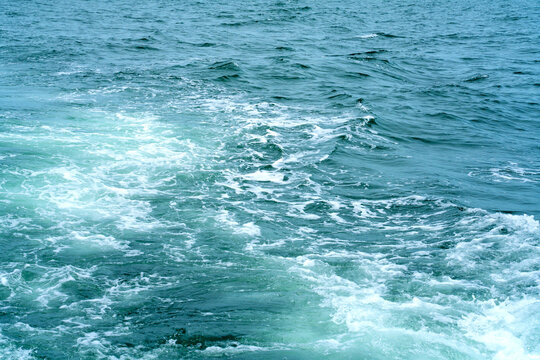 Churning turquoise ocean water with white foam and ripples. Dynamic sea surface capture showing boat wake and water movement. Ideal for nautical, vacation, and nature background concepts.