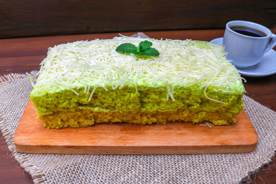 Delicious avocado flavored cake topped and filled with creamy frosting, generously covered with fine shredded cheese and garnished with fresh mint leaves served on a wooden board