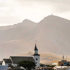 Nordic village with white church spire in front of a majestic mountain under warm sunlight © Quality by Simon