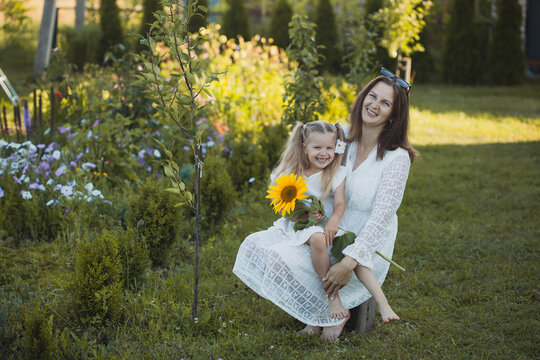 a cute five-year-old girl with mother in a white dress are playing in a green summer garden. happy childhood