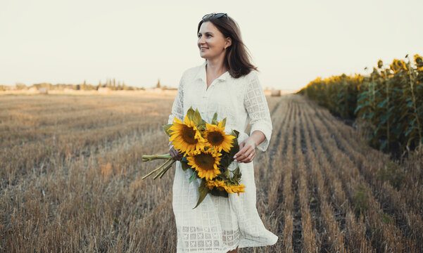 woman in a white dress holding a bouquet of wild flowers with sunflowers in a field
