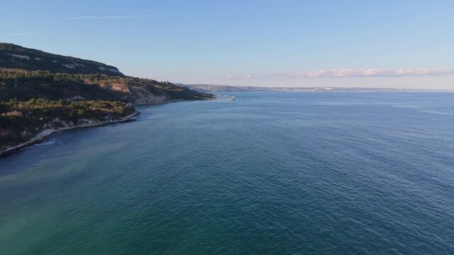 Wide aerial view of coastal headland surrounded by blue sea beneath a cloudless summer sky