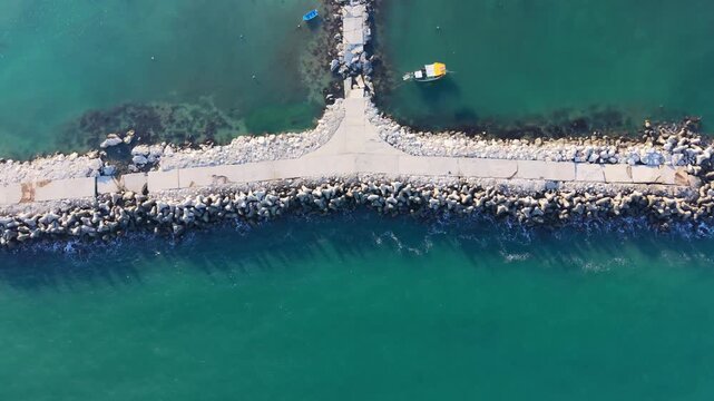 Aerial view of sandy beach path extending between turquoise sea water and rocky shoreline