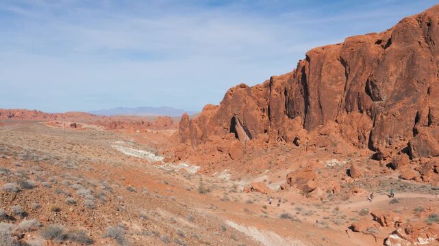 Panoramic view of desert canyon showing tourists walking along trail surrounded by impressive red sandstone formations in american valley of fire state park. Hiking in heat desert to red rock