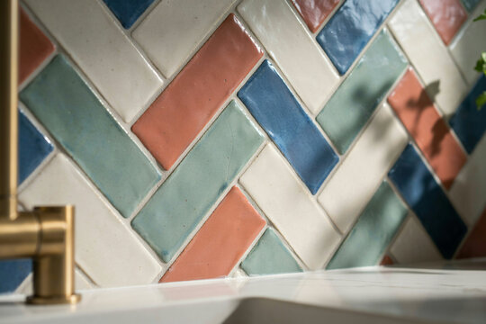 Kitchen backsplash featuring rectangular ceramic tiles arranged in a herringbone pattern with blue, green, white, and terracotta colors and brass tap