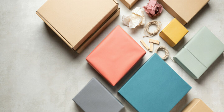 View of various cardboard shipping boxes and colorful wrapped parcels with twine string on a light gray concrete floor surface