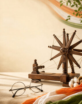 Miniature wooden spinning wheel charkha with round wire-rim glasses and tricolor fabric representing Indian independence and heritage themes