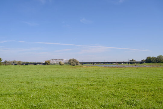 Wide view of a lush green meadow in the IJssel valley with the Westervoort railway bridge in the background