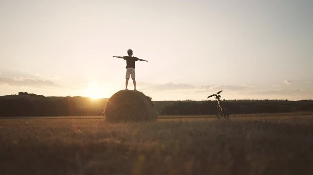 Little boy having fun when standing on haystack in fields, aerial panorama. Admiring sunrise, enjoying merry vacation or holidays in nature, picturesque rural scenery in agricultural region, farming