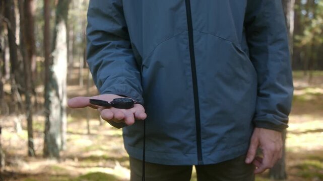 Unrecognizable male traveler wearing a jacket holding a magnetic compass in his hand and determining the direction of the north for orienteering in the woods while hiking on a sunny day