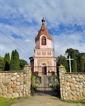 Symmetric view of an Orthodox church bell tower behind a stone wall and closed metal gate