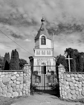 Monochrome symmetric view of an Orthodox church bell tower behind a stone wall and closed metal gate