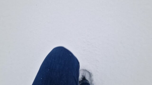 Top view of legs in winter boots and jeans walking through deep white snow. Video shows first person movement during a winter walk or hike. Close-up of legs making a path through fresh snow