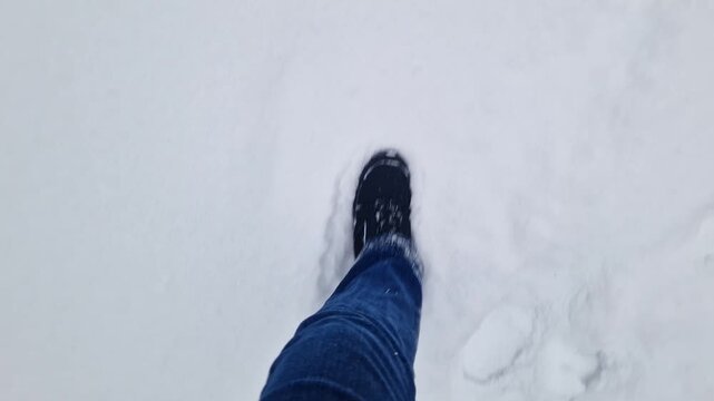 Top view of legs in winter boots and jeans walking through deep white snow. Video shows first person movement during a winter walk or hike. Close-up of legs making a path through fresh snow