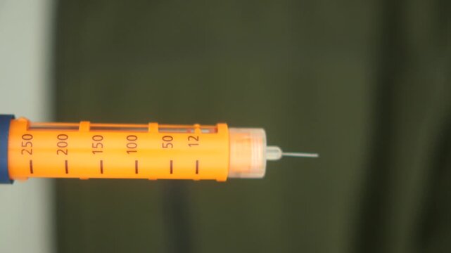 Horizontal close up of insulin pen injector being used to deliver dose for diabetic patient