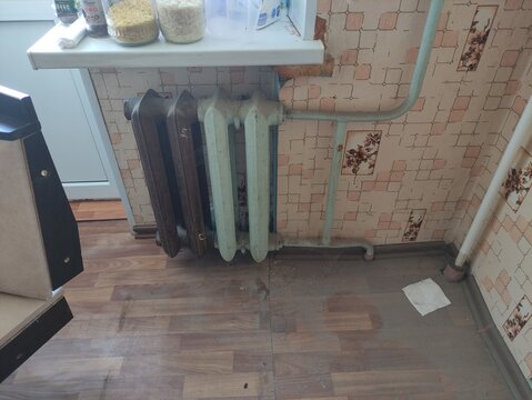Old cast iron radiators with green and brown paint on wooden floor in kitchen