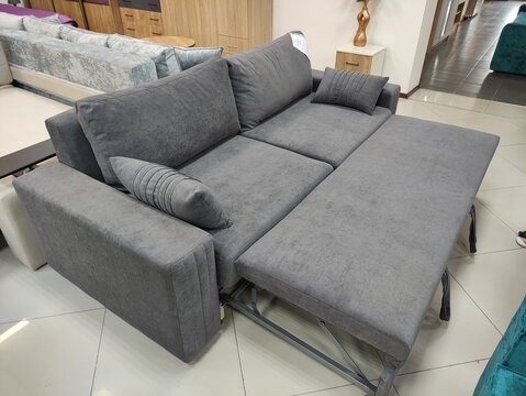 Grey fabric sofa bed with extended sleeping section and pillows in a furniture store