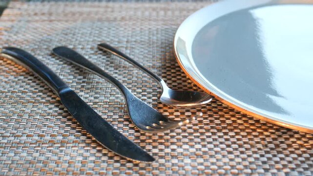 A close up video of a person taking away fork and knife from a neatly set dining table, leaving only spoon and plate on display