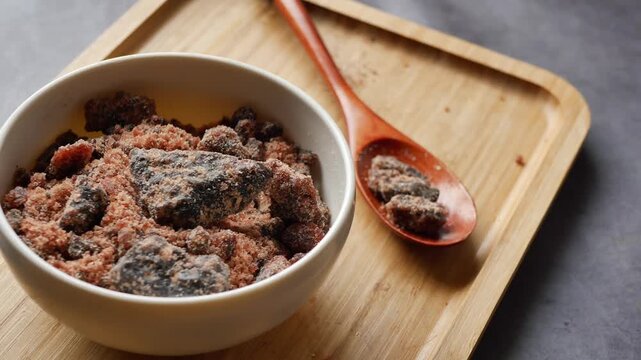 Slow motion close up of organic dark brown sugar chunks in ceramic bowl on wooden tray with wooden spoon