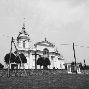 Monochrome low angle view of a classical Catholic church facade with columns, bell tower and stone fence