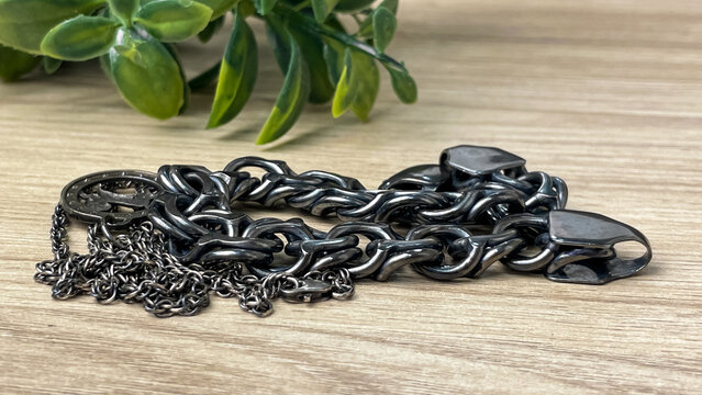 Tarnished silver chains lie on a wooden table next to a green plant. A scene suitable for topics such as jewelry care, metal restoration, and cleaning jewelry at home.