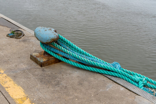 Thick nautical ropes secured to a weathered bollard on a concrete pier by the water