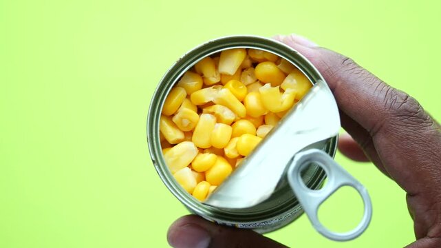 Close up of a hand opening a tin can filled with sweet corn kernels