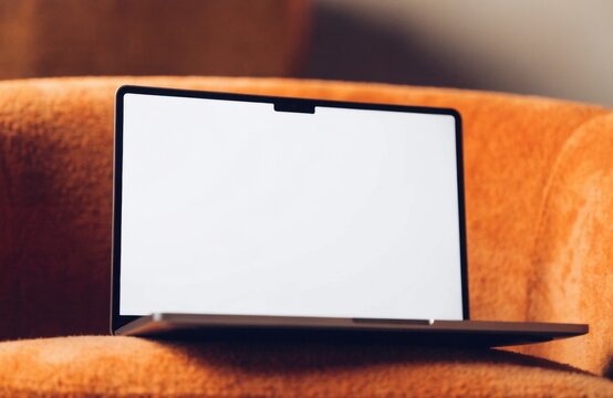 A sleek, dark grey laptop with a blank white screen rests on an orange textured surface