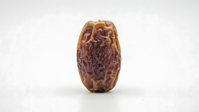 A single dried date fruit with a wrinkled brown skin and a textured surface isolated on a plain white background, for food