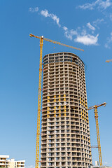 Modern high-rise building under construction with cranes against a blue sky © k_samurkas