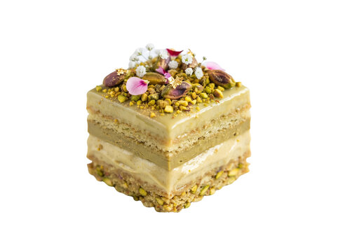 Gourmet pistachio layer cake with crushed nuts and floral petals, elegant square petit four pastry, luxury artisanal dessert isolated on white