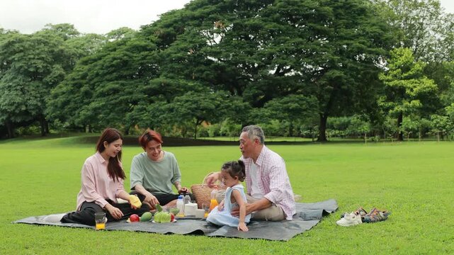 food and drinks. Happy Asian family having fun time on picnic at city nature park, outdoor activitie