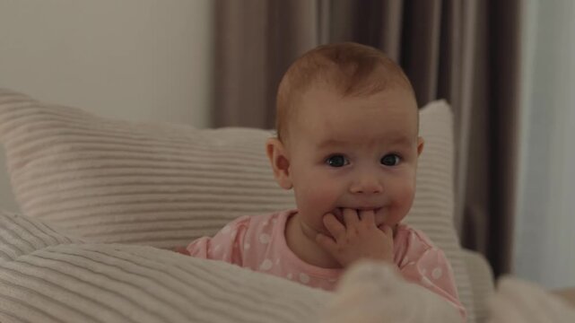 Infant doing tummy time on sofa chewing fingers