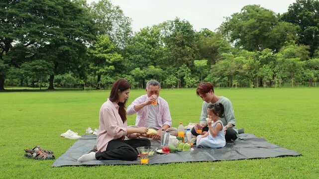 food and drinks. Happy Asian family having fun time on picnic at city nature park, outdoor activitie