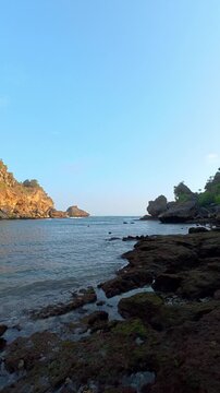 Vertical coastal view of rocky tropical cove beneath clear blue sky