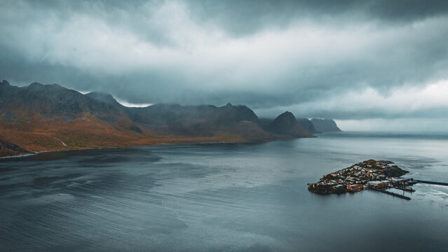 Dramatic aerial view of island village husoy surrounded by northern fjord and mountains under stormy cloudy sky with copy space