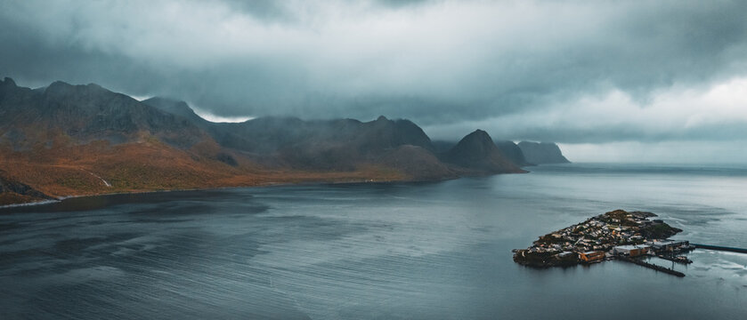 Dramatic aerial view of island village husoy surrounded by northern fjord and mountains under stormy cloudy sky with copy space