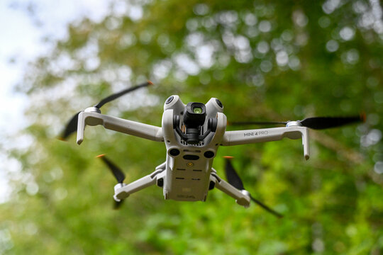 drone de loisirs en vol sur un fond de v&eacute;g&eacute;tation et de verdure. Mod&egrave;le DJI mini 4 pro avec cam&eacute;ra et nacelle, les 4 h&eacute;lices tournent au bout des bras pliables.