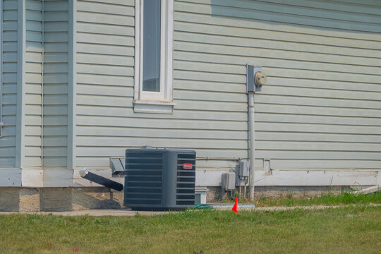 Calgary, Alberta, Canada. September 18, 2026. An air conditioning compressor unit installed outside a residential home wall with light green siding.