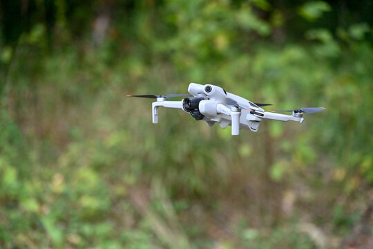 drone de loisirs en vol sur un fond de v&eacute;g&eacute;tation et de verdure. Mod&egrave;le DJI mini 4 pro avec cam&eacute;ra et nacelle, les 4 h&eacute;lices tournent au bout des bras pliables.